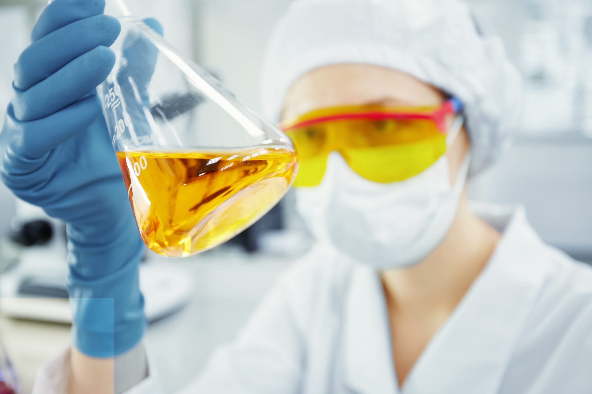 lose up portrait of young woman's hands holding test tube with yellow liquid. Medical researcher or doctor wearing surgical mask and safety glasses looking at glass tube while working in laboratory